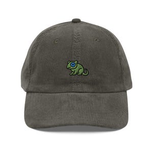 Può includere: Un cappello da baseball in velluto a coste verde scuro con una rana verde ricamata con un occhio blu.