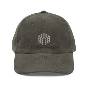 May include: A dark green corduroy baseball cap with a white embroidered geometric design on the front.