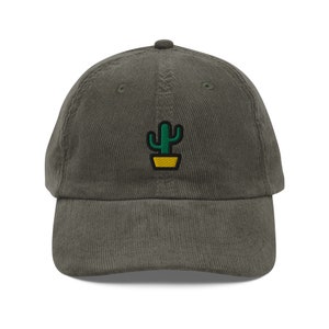 Op de afbeelding: Een donkergroene corduroy baseballpet met een geborduurd groene cactus in een gele pot.