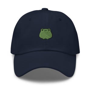 Könnte beinhalten: Eine marineblaue Baseballkappe mit einem grünen gestickten Frosch auf der Vorderseite.