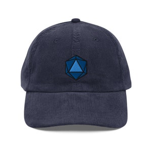 May include: A navy blue corduroy baseball cap with an embroidered blue and black geometric design on the front.
