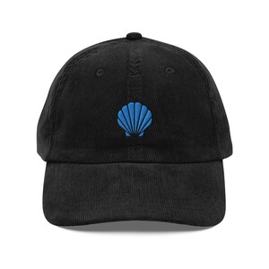 Peut inclure: Casquette de baseball en velours côtelé noir avec une broderie bleue en forme de coquillage. La casquette a une visière incurvée et une sangle réglable. Le coquillage est brodé sur le devant.