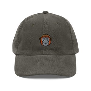 May include: A green corduroy baseball cap with an embroidered monkey face.