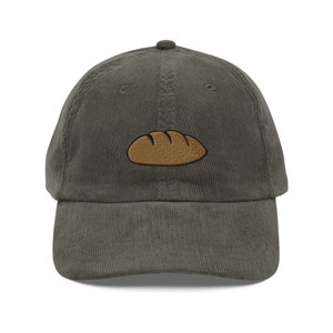 May include: A dark green corduroy baseball cap with an embroidered brown loaf of bread on the front.