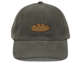 Op de afbeelding: Een donkergroene corduroy baseballpet met een geborduurd bruin brood op de voorkant.