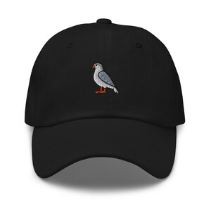 Può includere: Cappellino da baseball nero con un ricamo di un uccello. L'uccello ha piume grigie e bianche, becco e zampe arancioni. Il cappellino ha una visiera curva e un cinturino regolabile.