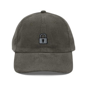 Op de afbeelding: Een groene corduroy baseballpet met een klein geborduurd hangslot in het midden.