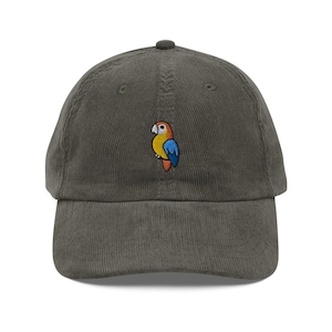 Könnte beinhalten: Eine grüne Cord-Baseballkappe mit einem gestickten Papageien-Design. Der Papagei ist gelb, orange und blau.