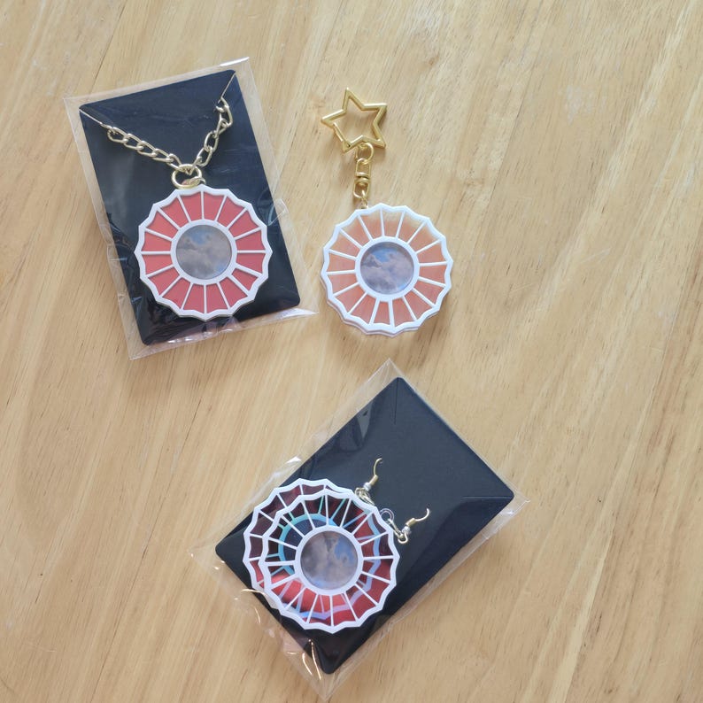 May include: A set of three jewelry pieces featuring a red, orange, and white flower design. The set includes a necklace, a keychain, and a pair of earrings.