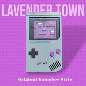 May include: A grey Game Boy handheld video game console against a purple background. The screen shows a pixelated image of a video game level. The console has a black directional pad, two purple buttons, and black and white start and select buttons.