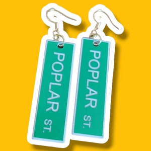 May include: A pair of green and white earrings with the text "POPLAR ST." on each earring.