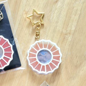 May include: A white and orange circular keychain with a star-shaped metal ring. The keychain features a picture of a cloudy sky in the center.