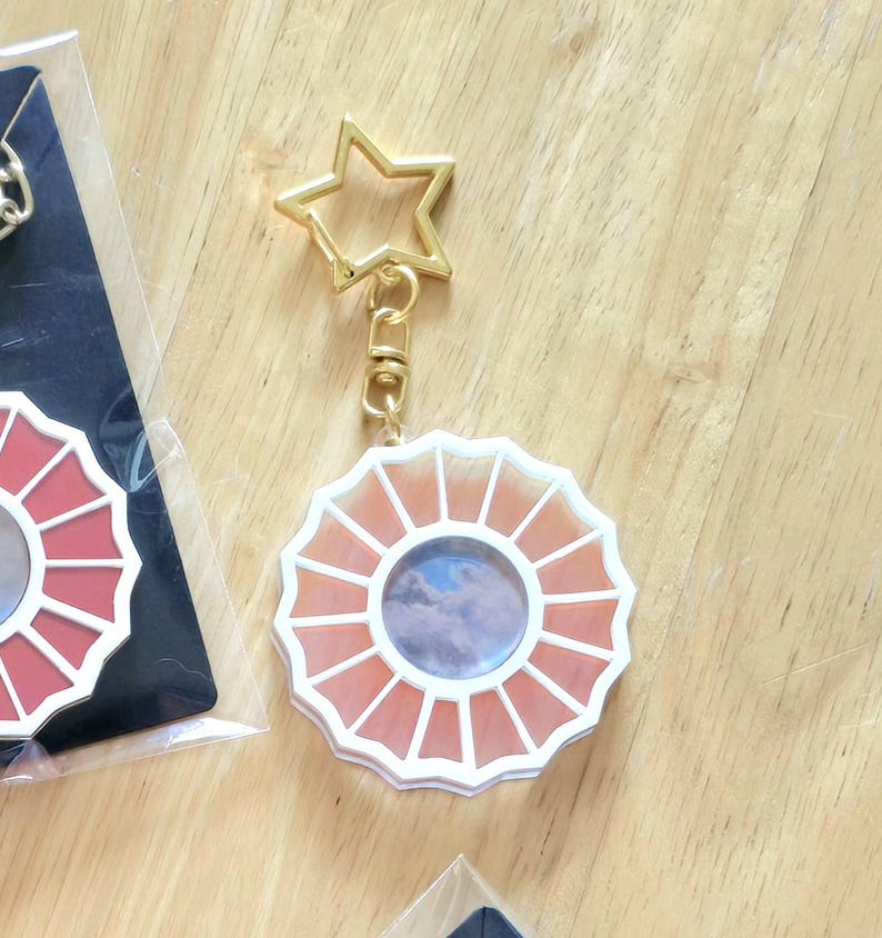 May include: A white and orange circular keychain with a star-shaped metal ring. The keychain features a picture of a cloudy sky in the center.
