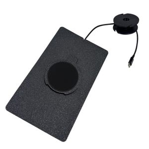 Puede incluir: Una base de carga rectangular negra con textura y una hendidura circular en el centro. Un cable negro fino se extiende desde el borde superior de la base, conect&aacute;ndose a un peque&ntilde;o componente de bobina circular negra con un conector USB-C.
