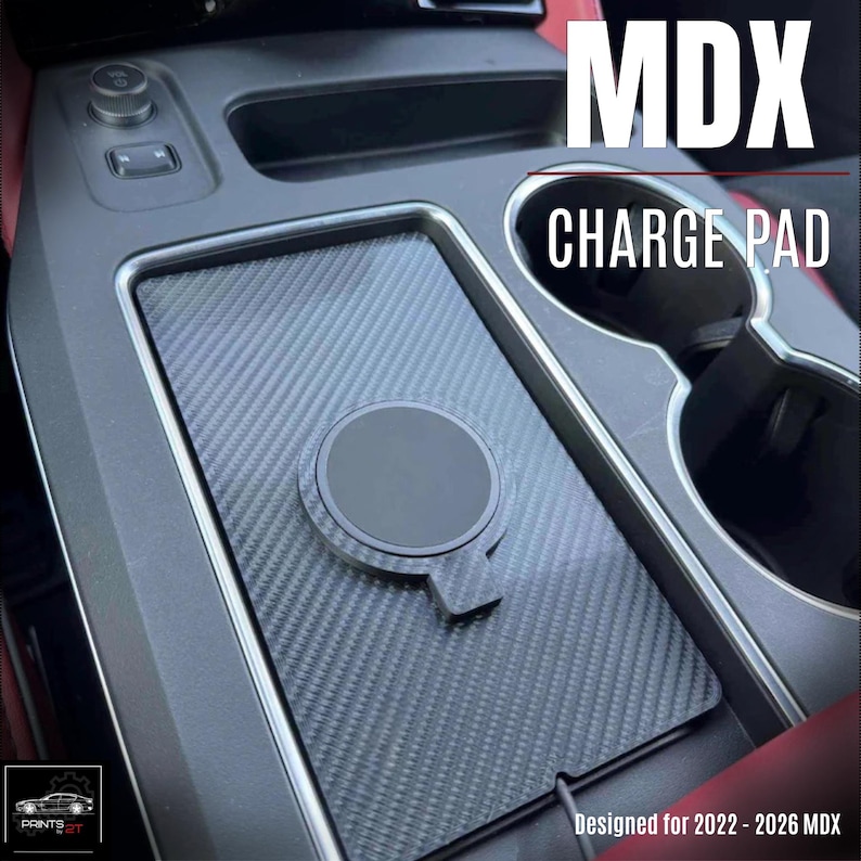 Puede incluir: Una base de carga inal&aacute;mbrica con textura de fibra de carbono negra instalada en la consola central de un veh&iacute;culo. La base cuenta con un &aacute;rea de carga magn&eacute;tica circular y est&aacute; etiquetada con el texto MDX CHARGE PAD y Designed for 2022 - 2026 MDX.