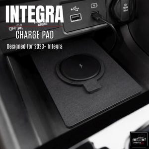 May include: Black wireless charging pad designed for 2023+ Integra vehicles. The pad has a circular charging area with a lightning bolt symbol. The text "CHARGE PAD" and "INTEGRA" are visible.