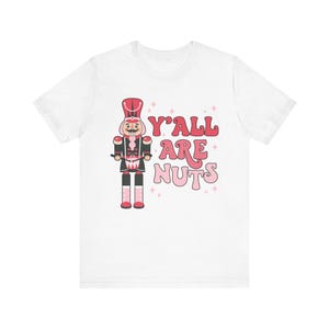 May include: White t-shirt with a pink and red illustration of a nutcracker and the text "Y'all are nuts".