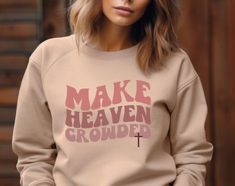 May include: A light beige sweatshirt with the text "MAKE HEAVEN CROWDED" in pink and red letters with a small black cross underneath.