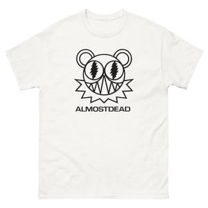 May include: White t-shirt featuring a black graphic of a bear-like face with lightning bolt eyes and a jagged mouth. The word "ALMOSTDEAD" is printed below the graphic in black.