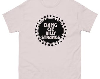 May include: A light pink t-shirt with a crew neck. The front features a black circular design with the text "DANG OL' BILLY STRANGS" surrounded by a ring of stars. The shirt is made of a soft, comfortable material.