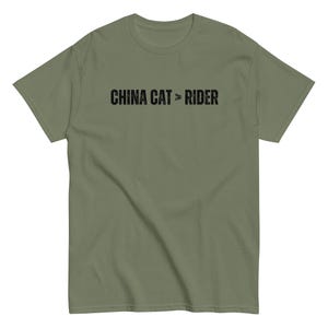 May include: Olive green t-shirt with the text "CHINA CAT > RIDER" printed in black. The shirt has short sleeves and a crew neck. The text is centered on the chest.
