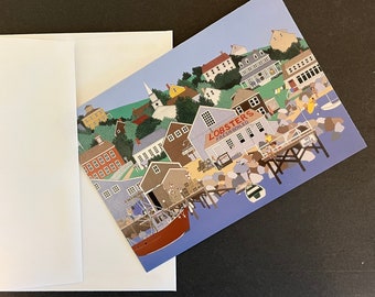 May include: A postcard featuring a coastal town scene with a harbor, buildings, and a lobster boat. The postcard is next to a white envelope. The postcard has the text "Lobsters Fresh Boiled".