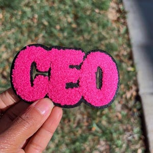 May include: Pink felt patch with the word "CEO" in black outlined letters.