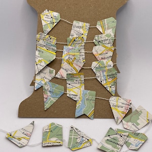 Puede incluir: Una guirnalda de cuerda blanca con banderas triangulares hechas de mapas de Berlín, Alemania. Las banderas están enhebradas en un carrete de cartón marrón.