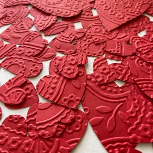 May include: A collection of red paper hearts with a patterned design. The hearts are scattered on a white surface.
