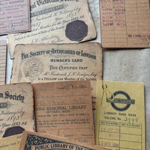 May include: A collection of vintage paper ephemera including library borrowing cards, membership cards for the Victorian Society and Society of Antiquaries of London, and a London Transport library bookmark, all featuring aged paper and printed text.