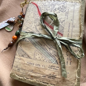 May include: A vintage-style journal with a map cover. The journal is bound with a green fabric and has a brass clasp. The map is of Leeds, Yorkshire, England and includes the text "YORKS. CCII. 11. LEEDS PH. PAICE 6/8NET."