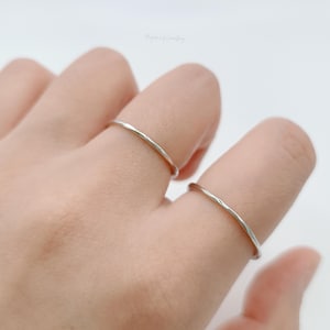 May include: Two thin silver rings on a person's fingers. The rings are simple and delicate, with a slightly twisted design.