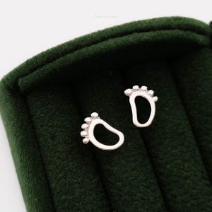 May include: A pair of silver baby footprint earrings. The earrings are small and delicate, and they are perfect for a new mom or a baby shower gift.