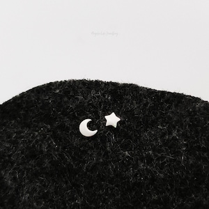May include: A pair of silver earrings featuring a crescent moon and a five-pointed star. The earrings are on a black surface.