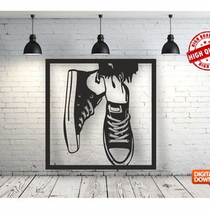 May include: Black and white silhouette of a pair of sneakers hanging from a wall mounted frame. The sneakers are tied and the laces are visible. The frame is square and has a black border.