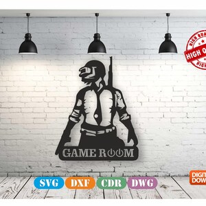 Könnte beinhalten: Schwarze und weiße Silhouette eines Videospielcharakters, der eine Waffe hält, mit dem Text "GAME ROOM" darunter. Das Bild befindet sich an einer weißen Backsteinwand mit drei schwarzen Pendelleuchten darüber. Das Bild ist zum digitalen Download in den Formaten SVG, DXF, CDR und DWG verfügbar.