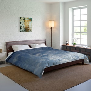 May include: A bed with a dark brown wooden frame and a blue and white comforter with a cloud design. The room has a white brick wall, a brown rug, and a floor lamp. An abstract painting hangs on the wall.