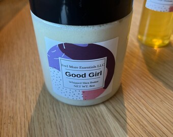 May include: A white jar with a black lid containing whipped shea butter. The jar has a label that says "Feel More Essentials LLC" and "Good Girl Whipped Shea Butter NET WT. 8oz".