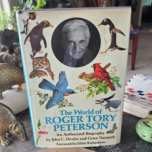 May include: A book titled "The World of Roger Tory Peterson: An Authorized Biography" by John C. Devlin and Grace Naismith with a foreword by Elliot Richardson. The cover features a portrait of Roger Tory Peterson and illustrations of birds, including penguins, owls, and a bluebird.