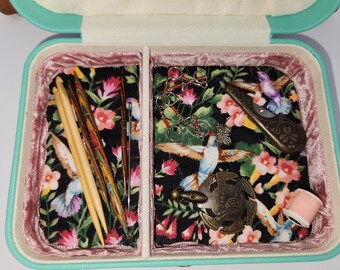 May include: A teal travel sewing kit with a floral print lining. The kit contains a variety of sewing tools, including needles, thread, and a small pair of scissors.