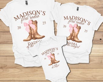 May include: White t-shirts and a onesie with a rodeo theme. Each shirt features the text "MADISON'S first rodeo" with a pair of brown cowboy boots and a pink bow. The onesie reads "I AM the cowgirl".