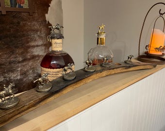 May include: A display featuring two bottles of liquor with decorative horse-themed stoppers. A wooden plank holds several small horse figurines. A candle holder with a horse silhouette is also present, creating a rustic, equestrian theme.