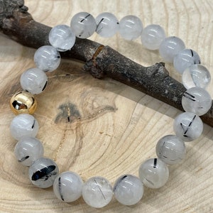 Peut inclure: Un bracelet composé de perles de quartz clair avec des inclusions de tourmaline noire. Le bracelet a un fermoir doré.