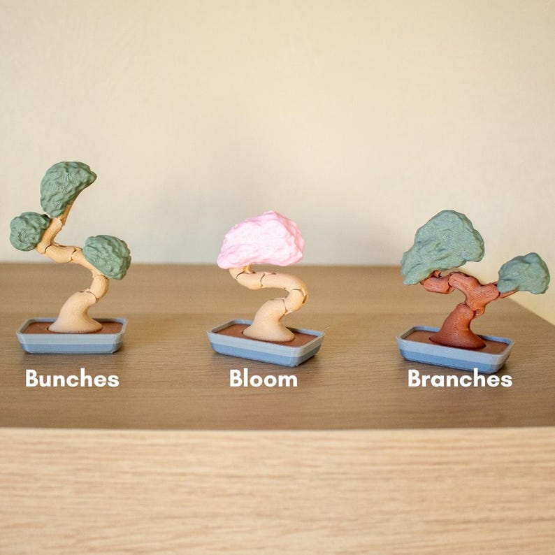 May include: Three miniature bonsai trees in different colors. The tree on the left has green foliage and is labeled "Bunches". The middle tree has pink foliage and is labeled "Bloom". The tree on the right has brown foliage and is labeled "Branches".