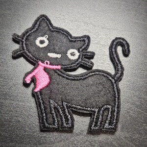 May include: Black cat felt patch with white eyes and a pink bow. The cat has a stitched outline. A whimsical design, ideal for adding to clothing or accessories. The patch is made of felt.
