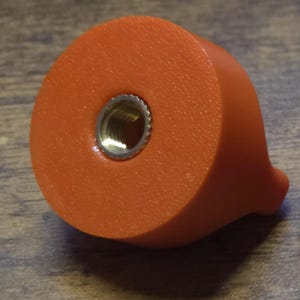 May include: Two orange plastic knobs with a threaded hole in the center of one knob. The knobs are used for adjusting or tightening something.