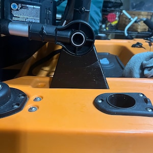 Pu&ograve; includere: Un supporto per sedile da kayak nero con un braccio girevole, fissato a un kayak arancione brillante. Il supporto &egrave; in metallo e plastica e ha una base nera.