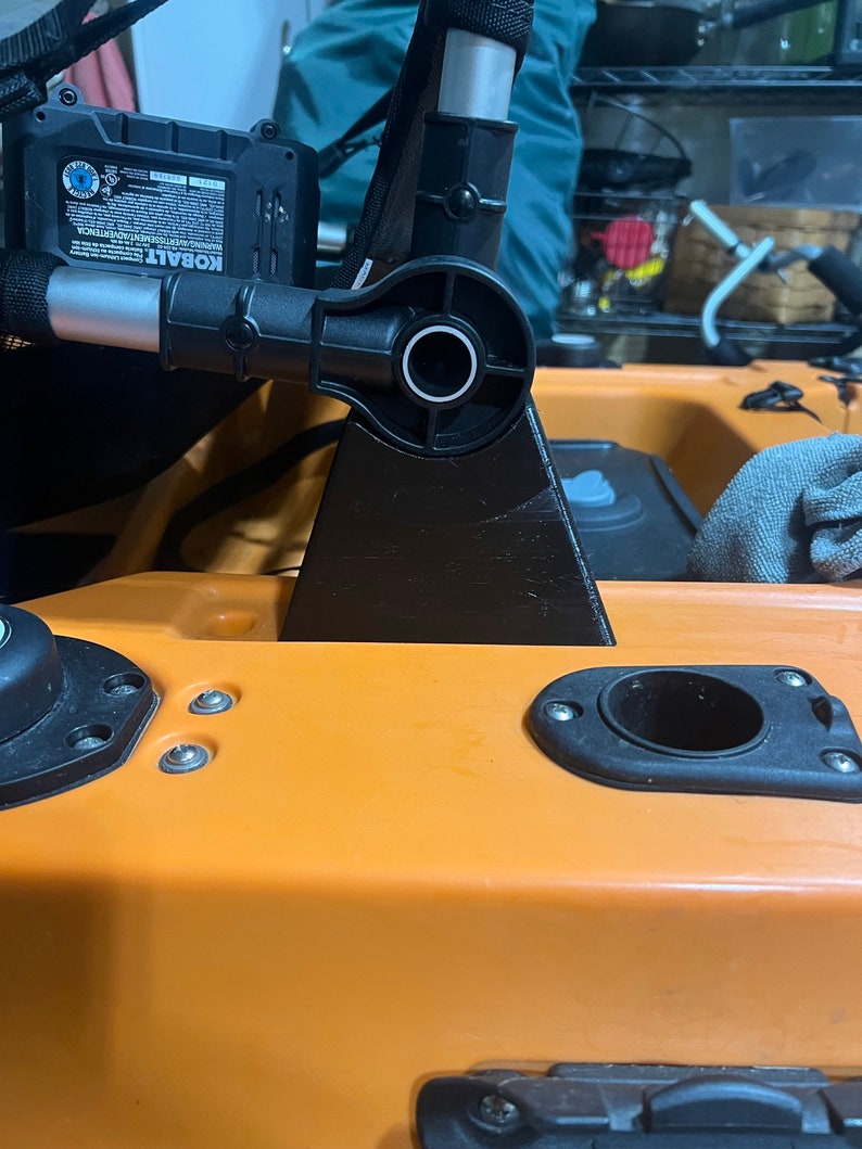 Pu&ograve; includere: Un supporto per sedile da kayak nero con un braccio girevole, fissato a un kayak arancione brillante. Il supporto &egrave; in metallo e plastica e ha una base nera.