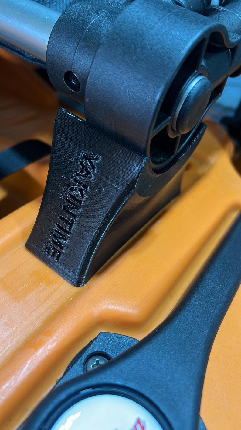 Pu&ograve; includere: Primo piano di un attacco per passeggino in plastica nera con la scritta "ULTIMATE" stampata su di esso. L'attacco &egrave; fissato a un passeggino con una maniglia nera e un telaio arancione.