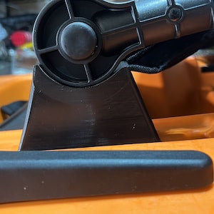 Pu&ograve; includere: Primo piano di un attacco per sedile da kayak nero con una manopola girevole. L'attacco &egrave; montato su un kayak arancione brillante.